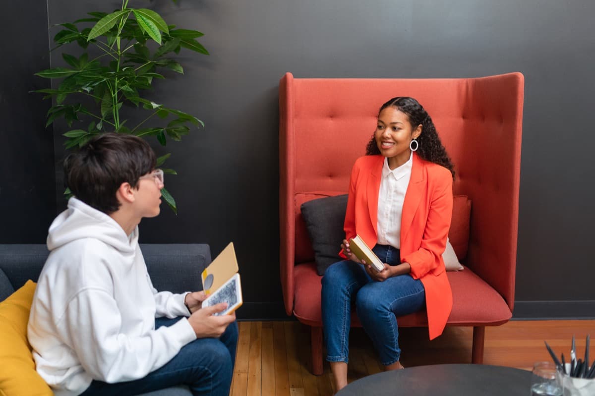 A mentor in an orange jacket talking with a teen