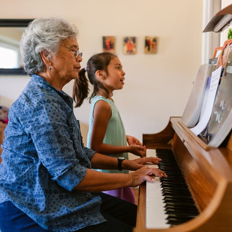 A child learning piano alongside an older mentor